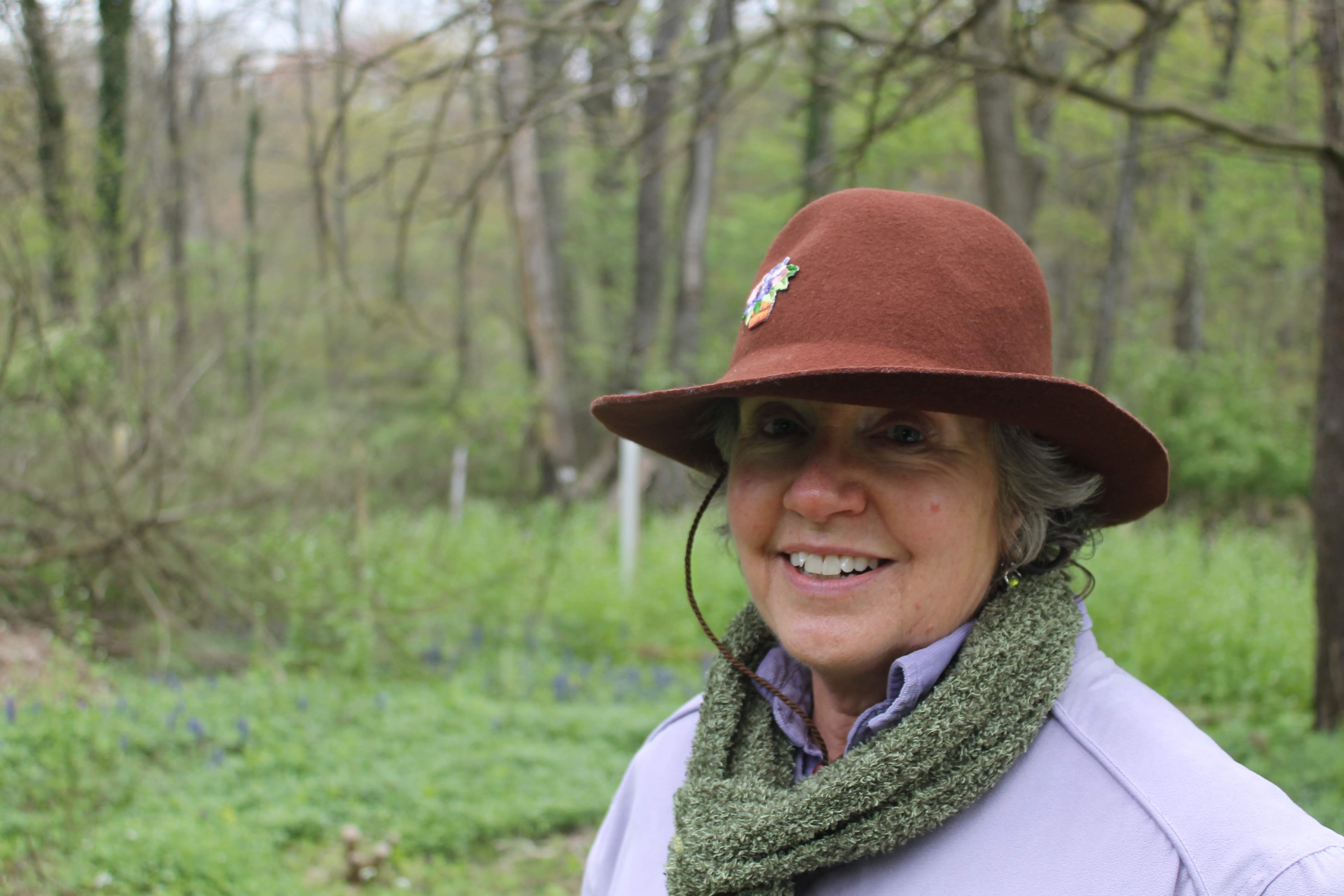 Smiling woman outdoors wearing a brown hat and green scarf.
