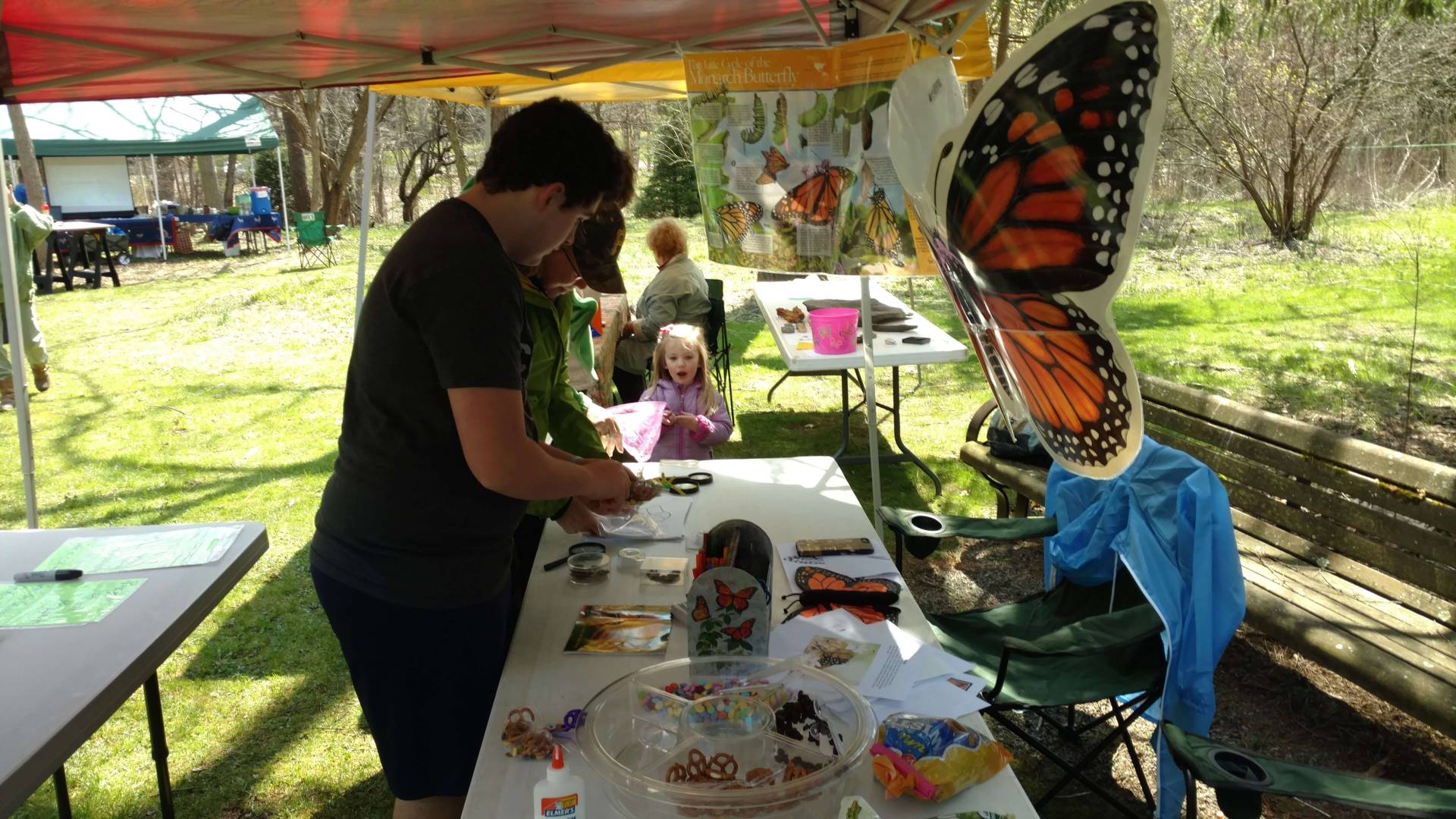 Person painting at an outdoor craft table under a colorful tent.