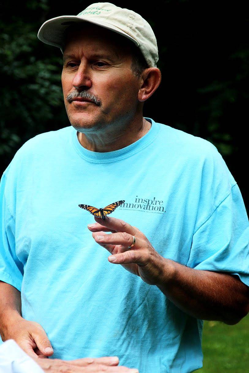 Man holding a butterfly on his finger outdoors.