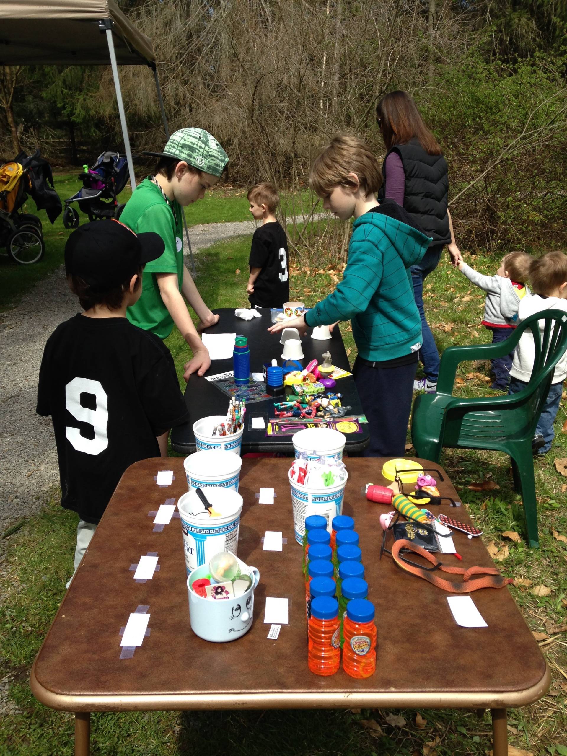Children and adults engaged in an outdoor craft activity with art supplies on a table.