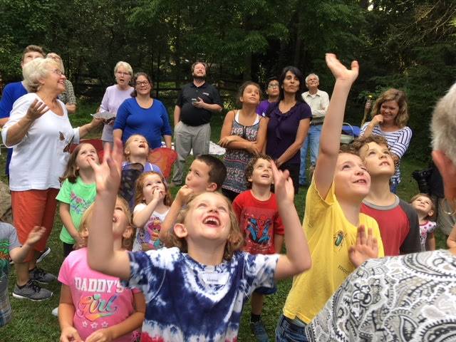 Children joyfully reaching up outdoors during a group activity.