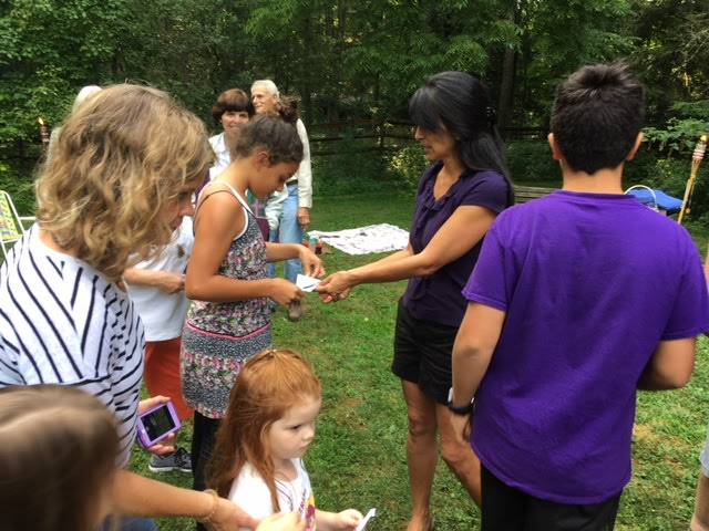 Children and adults exchanging papers outdoors on a grassy field.