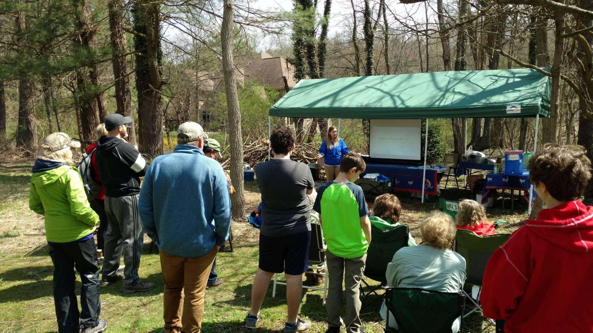 People gathered outdoors near a green-roofed structure in a wooded area.