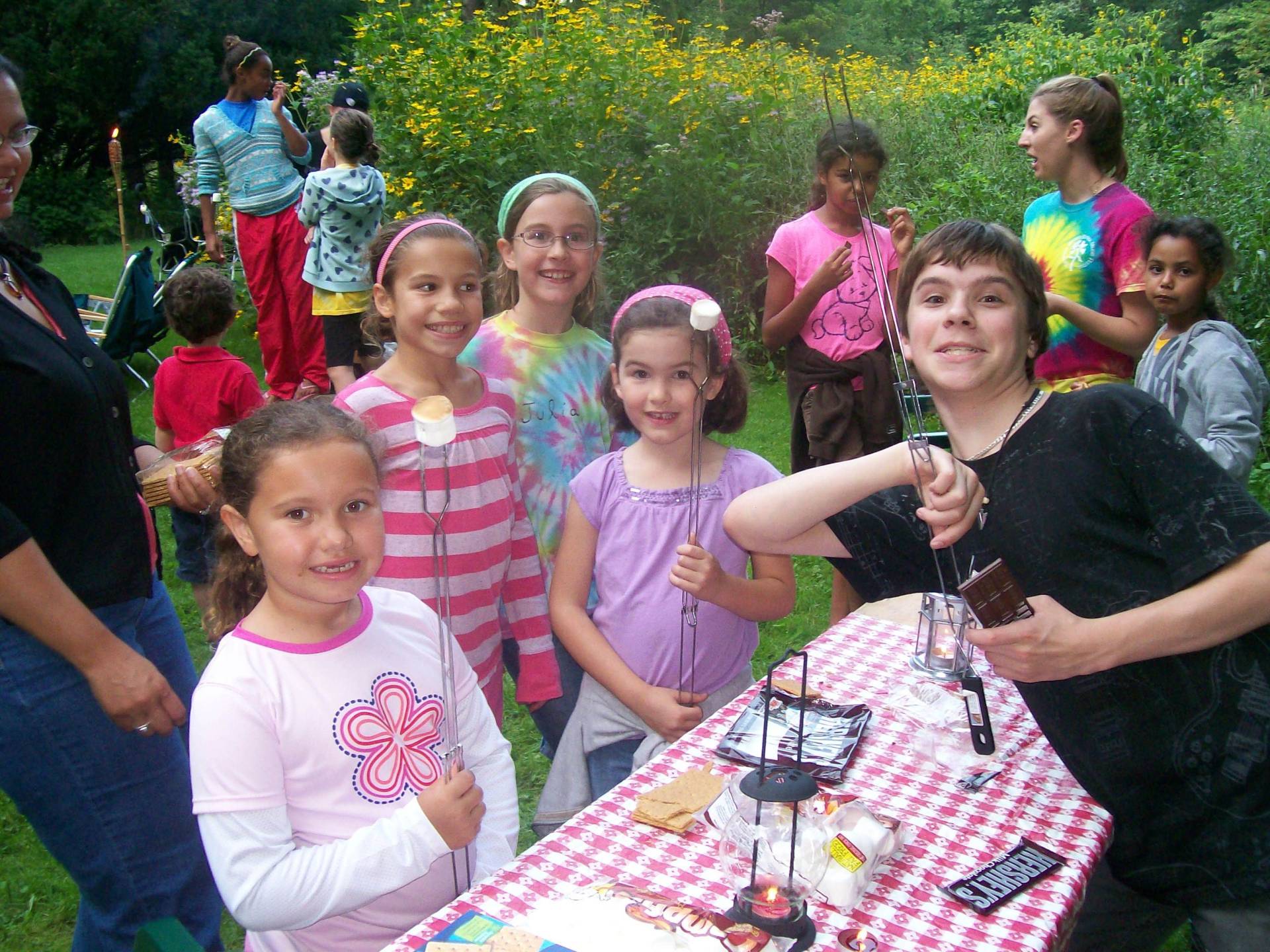 A group of children and a woman smiling outdoors at a picnic table.