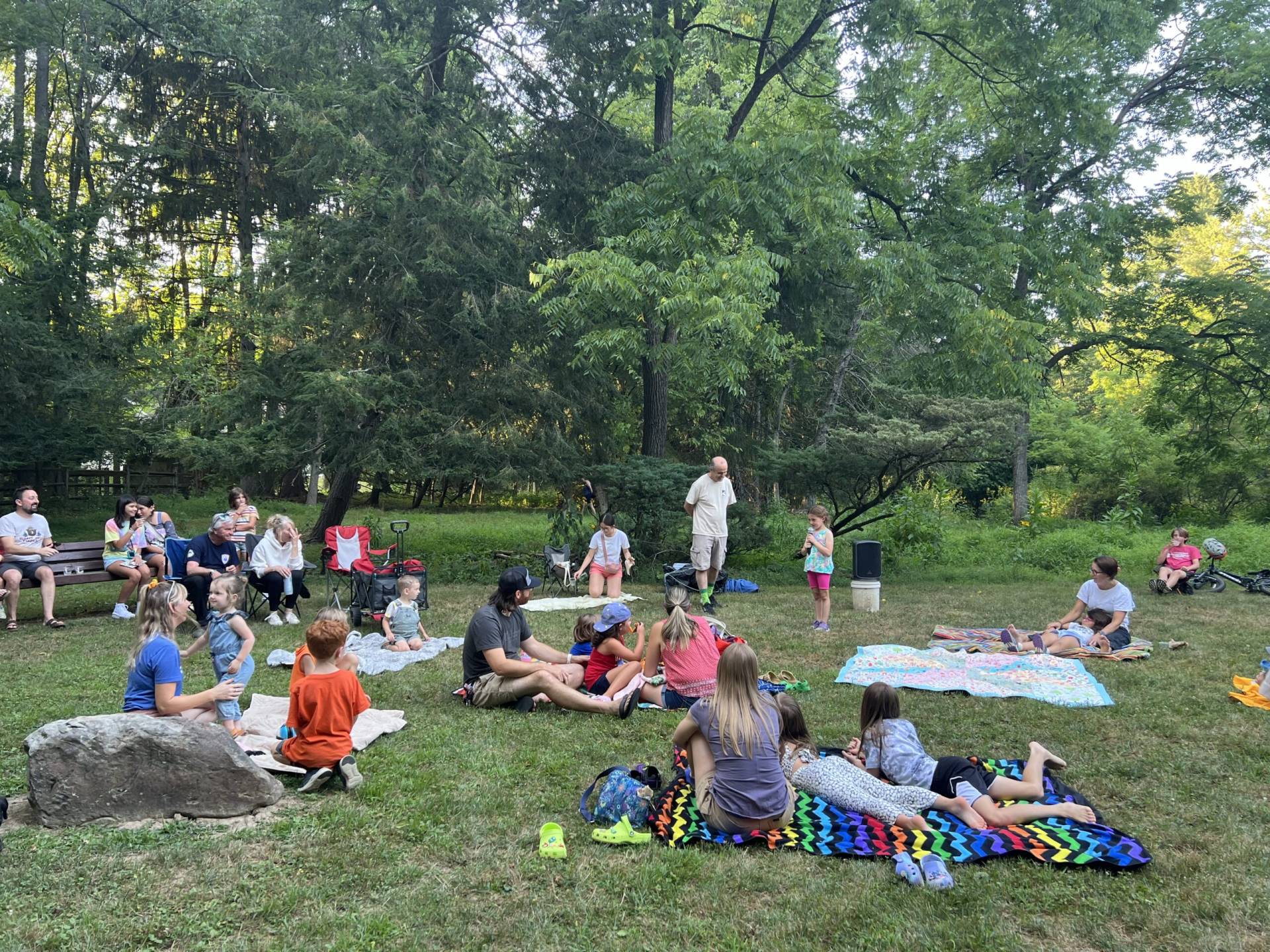Families and children enjoying an outdoor gathering in a wooded park.