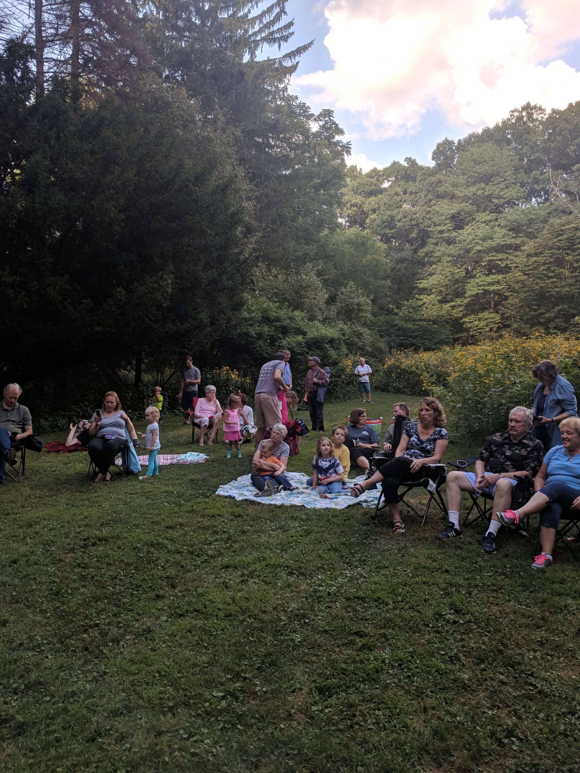 People gathered outdoors on a grassy area with trees in the background.