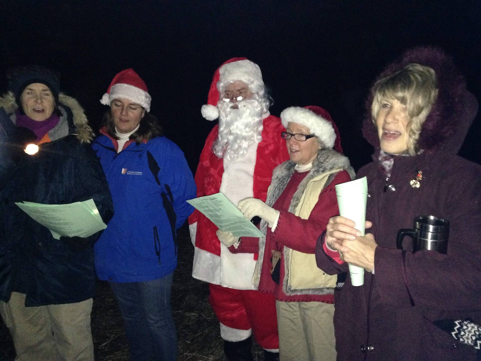 Group of people singing carols, including a person dressed as Santa Claus.