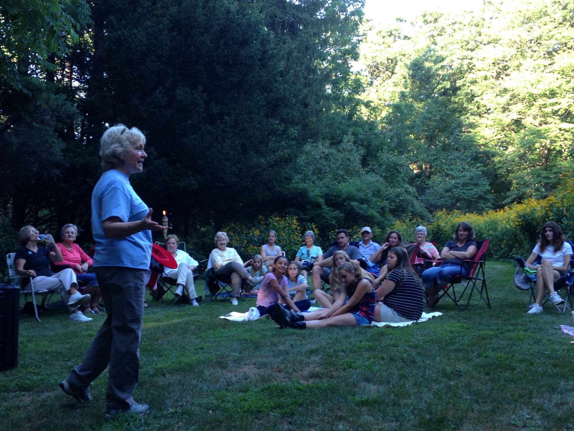 Group of people outdoors listening to a speaker in a natural setting.